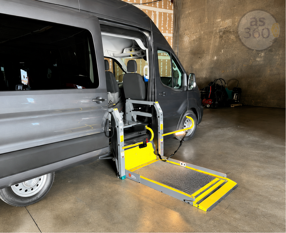 A gray minivan with its side door open, showing a deployed wheelchair lift ramp with yellow safety accents in a garage setting.