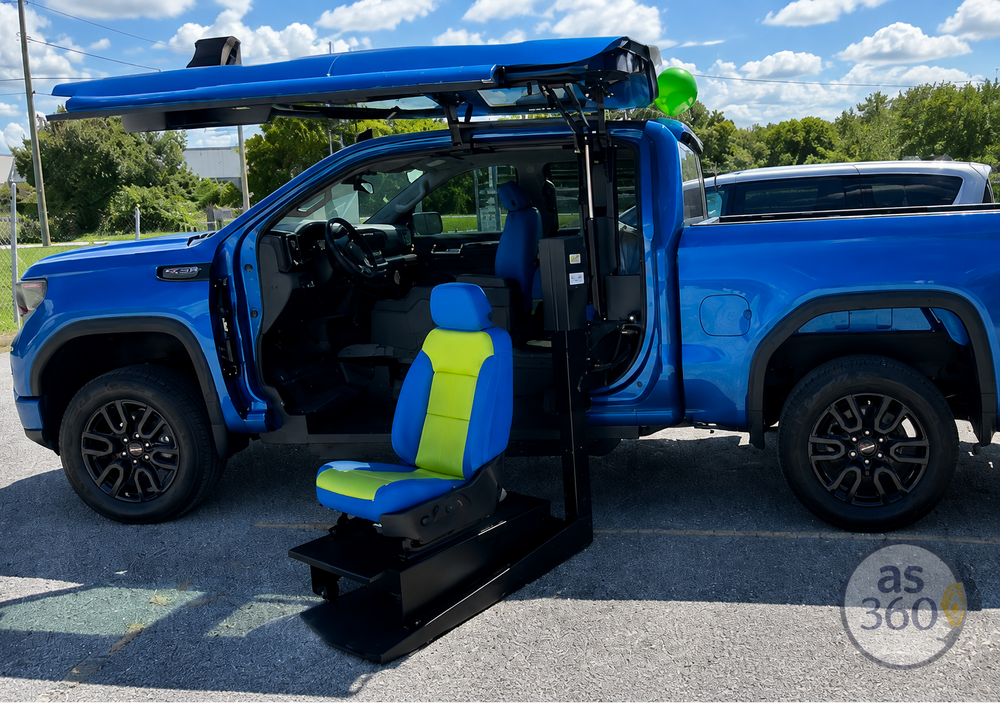 A blue and lime green vehicle seat lift mounted on a black frame, positioned outside a bright blue pickup truck with the driver's side door open, showing the seat elevated.