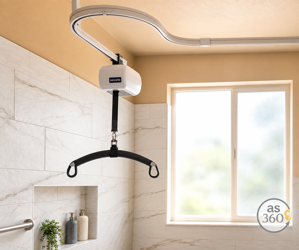 A ceiling lift system with a white motor unit, curved metal track, and black sling bar, installed in a tiled bathroom with a window.