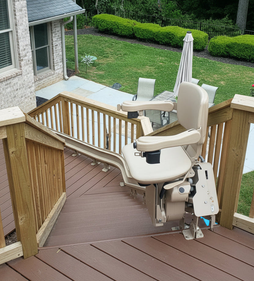 A curved stairlift installed on an outdoor deck. The chair lift in beige, mounted on a brown wooden deck and overlooking a backyard with green grass and trees.