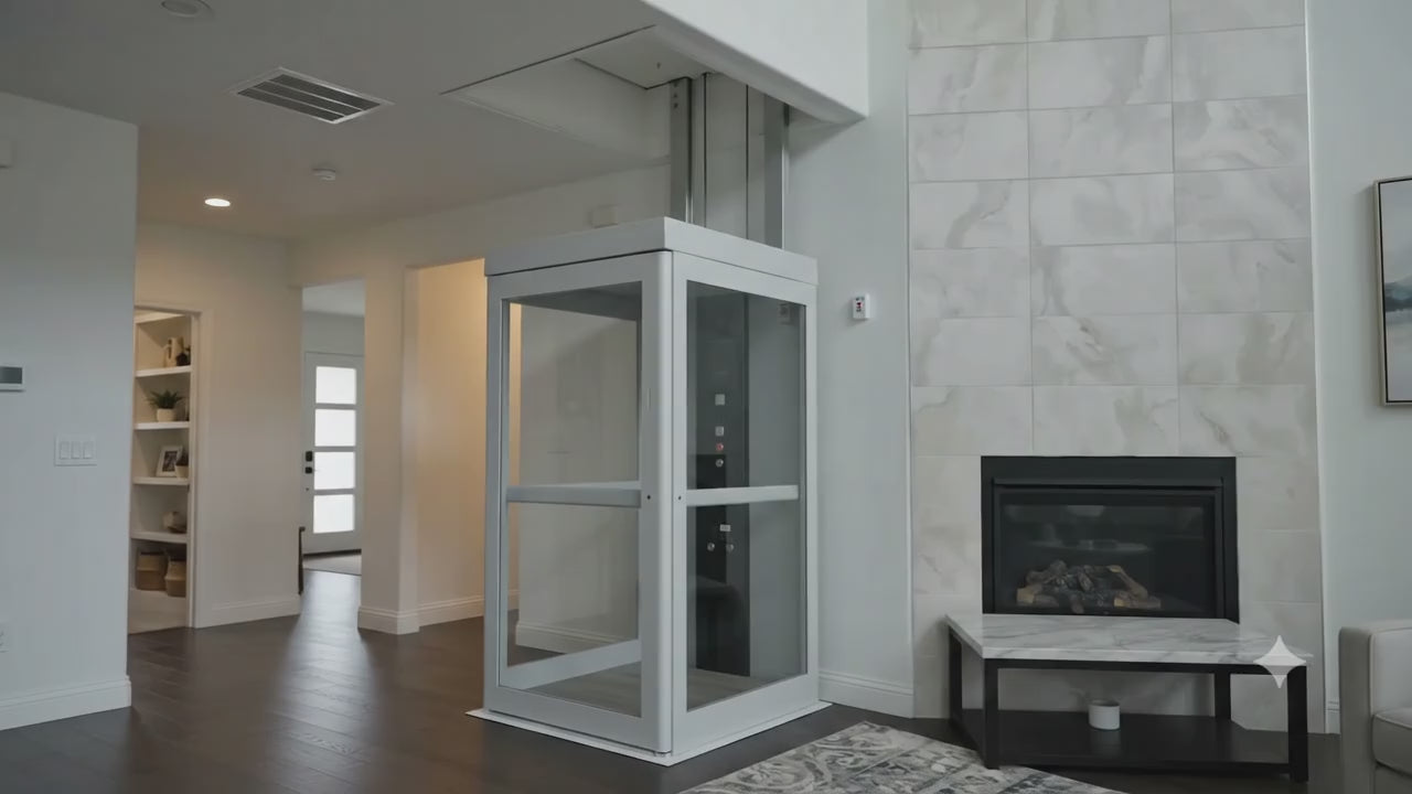 A compact glass-paneled home elevator with a white metal frame, handrail, and control panel. The video opens on the main floor, where the elevator is installed beside a stone fireplace in a living area with hardwood floors, a bookshelf, and front door visible nearby. The scene transitions to the elevator's upper-floor landing, an open carpeted room with two closet doors and a large window opening. No spoken narration; instrumental background music plays throughout.